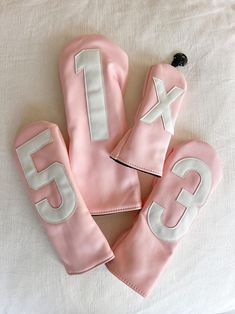 three pink mitts with white letters on them sitting on a bed next to each other