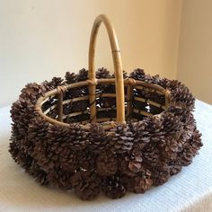 a basket made out of pine cones sitting on top of a white cloth covered table