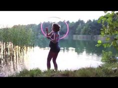 a woman standing in front of a lake holding a pink hula hoop