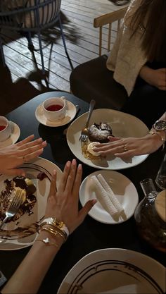 several people sitting at a table eating desserts and drinking tea, with their hands on the plates