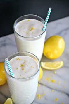 two glasses filled with lemonade sitting on top of a table next to sliced lemons