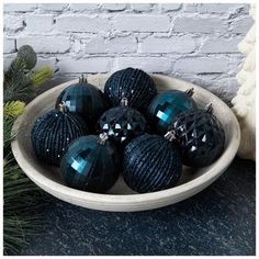 a bowl filled with black christmas ornaments on top of a table next to a white brick wall