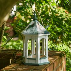 a small white lantern sitting on top of a brick wall next to green plants and trees