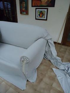 a white couch is covered by a sheet in front of some pictures on the wall