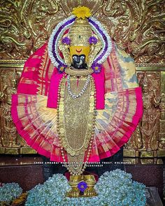 an idol is displayed in front of a gold wall with flowers and other decorations on it