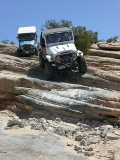 two jeeps driving on rocky terrain with trees in the background