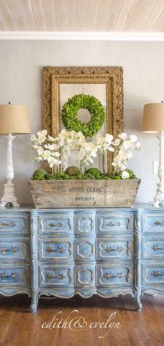 a blue dresser with flowers and a wreath on top