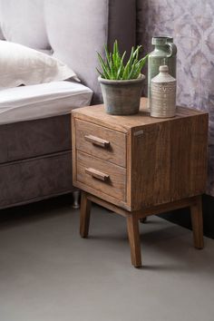 a small potted plant sitting on top of a wooden table next to a bed