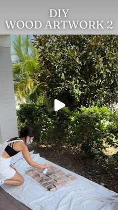 a woman sitting on top of a white sheet covered ground next to trees and bushes