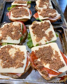 several sandwiches with meat and cheese are on a baking sheet, ready to be eaten