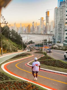 a man walking down a winding road in front of tall buildings and the city skyline