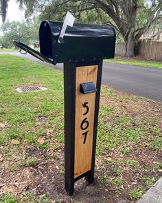 a mailbox sitting in the grass next to a tree and road with numbers painted on it