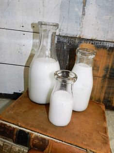 three glass bottles filled with milk sitting on top of a wooden table next to an old book