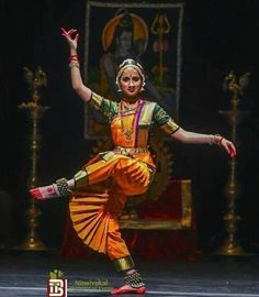 a woman in an orange and yellow outfit is doing a dance move with her arms outstretched