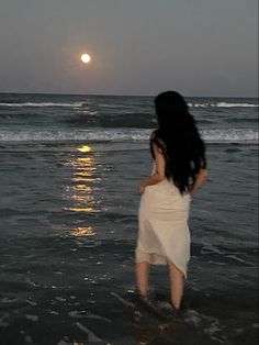 a woman walking into the ocean at sunset