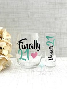 two wine glasses sitting next to each other on top of a wooden table with flowers in the background