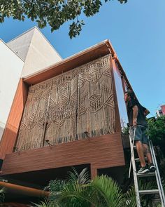 a man standing on a ladder next to a tall building with a wooden structure in front of it