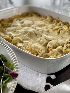 a casserole dish with meat and vegetables in it on a table next to silverware