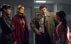 three people standing in an office with one person wearing a trench coat and the other looking at something