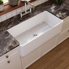 a white kitchen sink sitting on top of a counter next to a potted plant