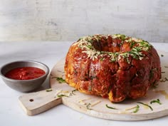 a bundt cake sitting on top of a cutting board next to a bowl of sauce