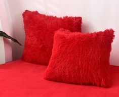 two red pillows sitting on top of a bed next to a plant in a vase