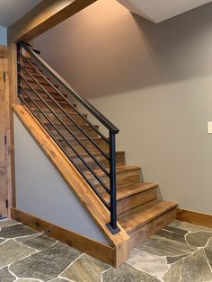 a wooden stair case with metal handrails in a home entryway area that has stone flooring and gray walls