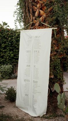 a large white banner hanging from the side of a tree next to a plant filled with leaves