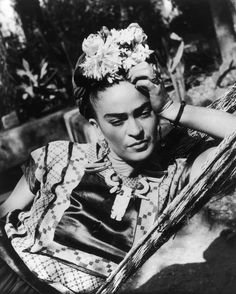 an old photo of a woman with flowers on her head sitting in a chair and looking at the camera