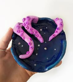 a hand holding a blue and purple plate with pink octopus decorations on the top,