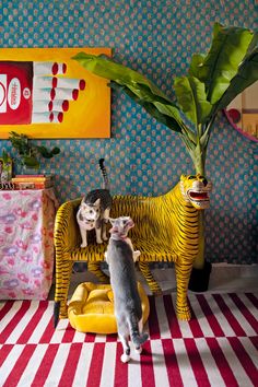 two cats standing on top of a yellow chair next to a potted palm tree