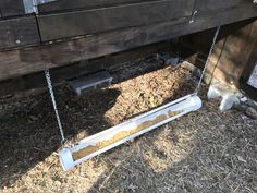 a bird feeder hanging from the side of a wooden fence next to grass and dirt