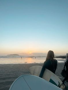 two people are walking on the beach with surfboards in hand and one person is holding a surfboard