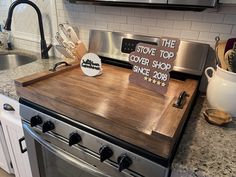 a wooden cutting board on top of an oven in a kitchen with stainless steel appliances