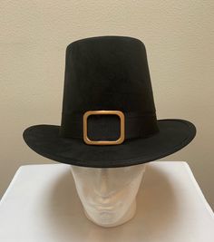 a white mannequin head wearing a black hat with a gold buckle on it