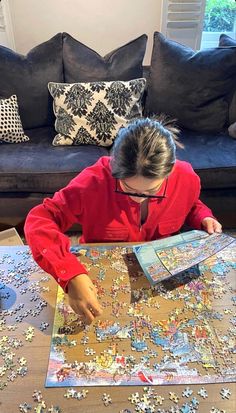 a person sitting at a table with a large puzzle on it's surface and looking down