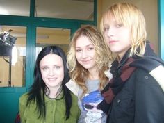 three young women standing next to each other in front of a green door and window