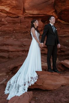 a bride and groom hold hands while standing on rocks in front of red rock formations