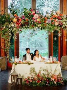 a couple sitting at a table with flowers and candles