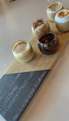 four different desserts on a wooden board sitting on a white counter top with chalk writing