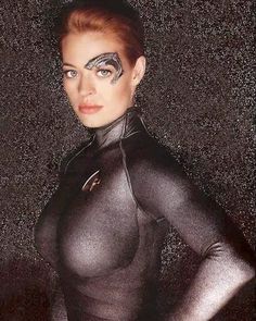 a woman in black catsuit posing with her hands on her hips and painted face