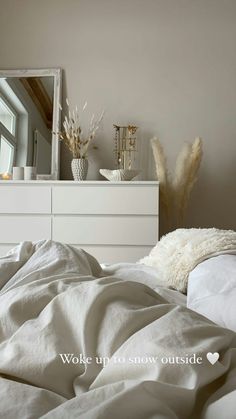 a white bed sitting next to a dresser with a mirror on it's side