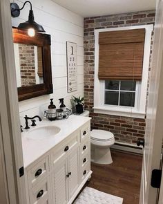 a white bathroom with brick walls and wood flooring is pictured in this image from the doorway