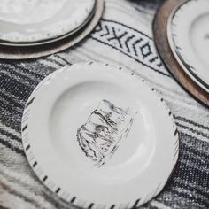 white plates with black designs on them sitting on a tablecloth covered table cloth in front of two wooden coasters