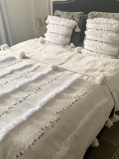 a white bed topped with lots of pillows next to a night stand in a bedroom