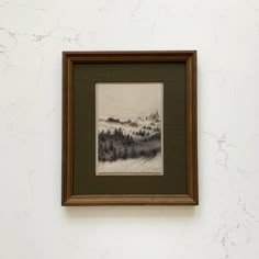 a painting hanging up on the wall above a framed object with an image of a forest in it