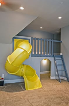 a yellow slide in the middle of a room with stairs and ladders on the wall