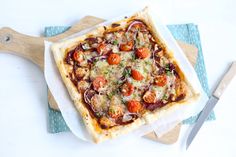 a square pizza sitting on top of a cutting board next to a wooden spatula