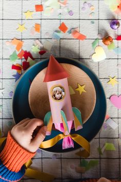 a person holding a paper rocket on top of a plate with confetti around it