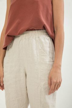 a woman is standing with her hands in her pockets and wearing a brown top that has an asymmetrical design on it